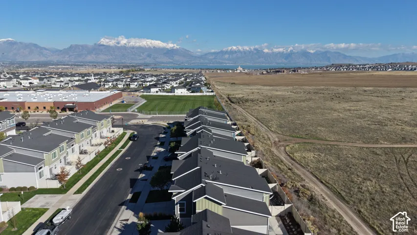 Aerial perspective of the residential community featuring multi-family structures with pitched roofs, paved streets, and a prominent mountain range backdrop