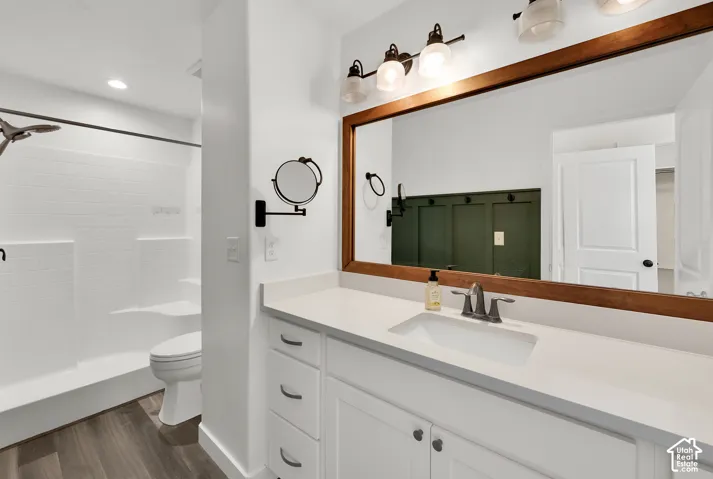 Bathroom featuring a white vanity with a solid-surface countertop, rectangular undermount sink, wood-framed mirror, and wood-finish flooring