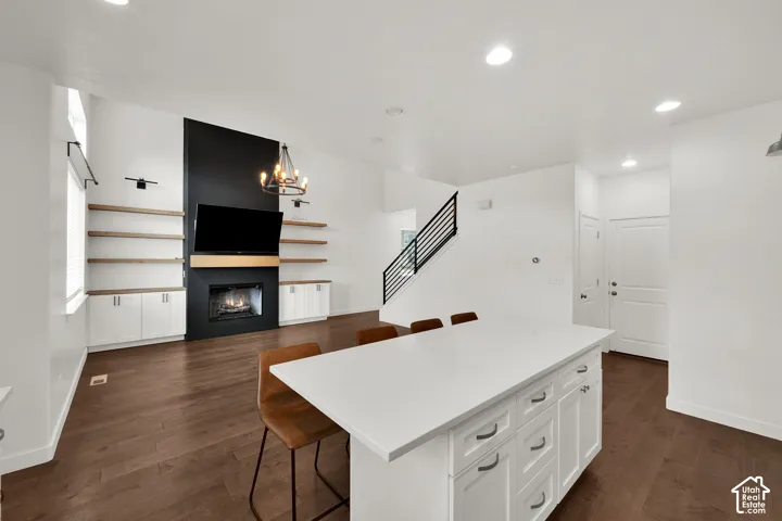 Open-concept interior featuring wood-finish flooring, a kitchen island with a white solid-surface countertop, and a fireplace with a black accent wall and built-in shelving