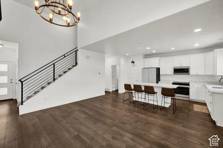 Open-concept interior featuring wood-finish flooring, white cabinetry, a large kitchen island, recessed lighting, and a staircase with a metal railing