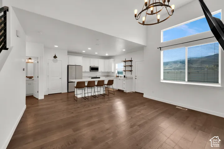 High-ceiling kitchen and common area featuring wood-finish flooring, white cabinetry, a center island, and large multi-pane windows
