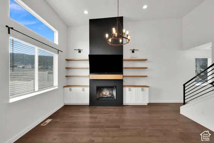 High-ceiling room featuring a floor-to-ceiling matte black fireplace, wood-finish shelving with built-in cabinetry, wood-finish flooring, and a decorative chandelier