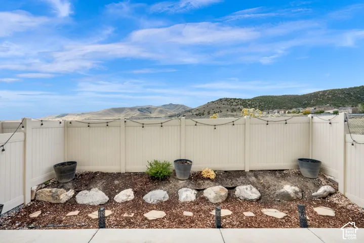 Backyard space featuring a light-colored privacy fence, stone-lined garden bed, concrete patio, and mountain backdrop