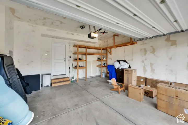 Attached garage featuring a concrete floor, built-in wooden wall shelving, and an exterior access door with wooden steps