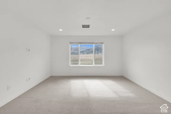Neutral-toned interior space featuring wall-to-wall carpeting, recessed ceiling lighting, and a large picture window showcasing a mountain landscape