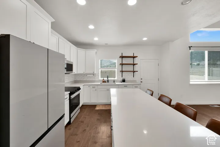 Kitchen featuring white shaker-style cabinetry, quartz countertops, a large center island, subway tile backsplash, and wood-finish flooring