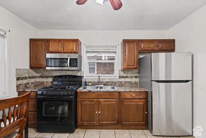 Kitchen featuring wood cabinetry, stone-patterned countertops, a tile backsplash, stainless steel appliances, and a double-basin stainless steel sink