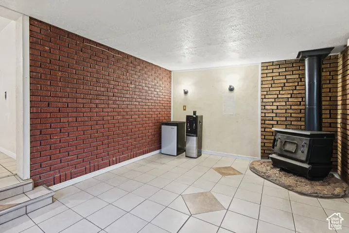 Interior space featuring red and earth-tone brick accent walls, tile flooring with diamond-patterned inlay, a wood-burning stove on a stone hearth, and dual wall-mounted light fixtures