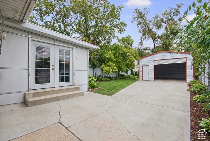 Exterior space featuring a concrete patio, French doors, detached garage, and mature landscaping