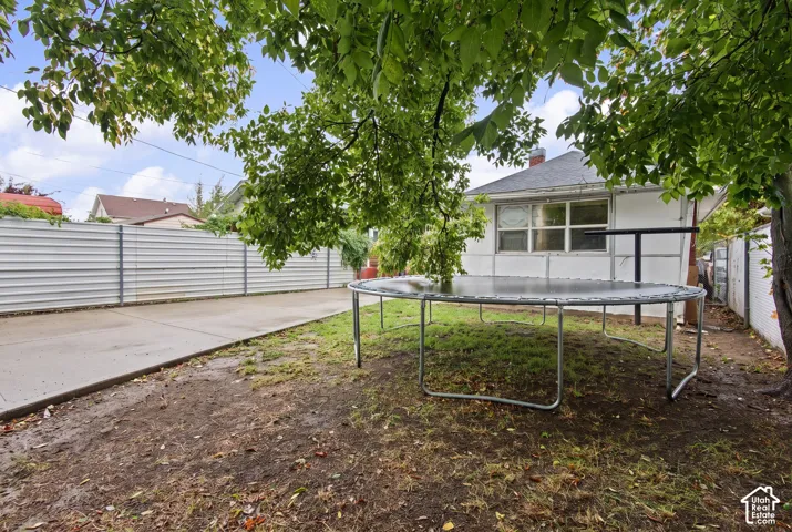 Exterior space featuring a concrete driveway, metal perimeter fencing, and mature tree canopy