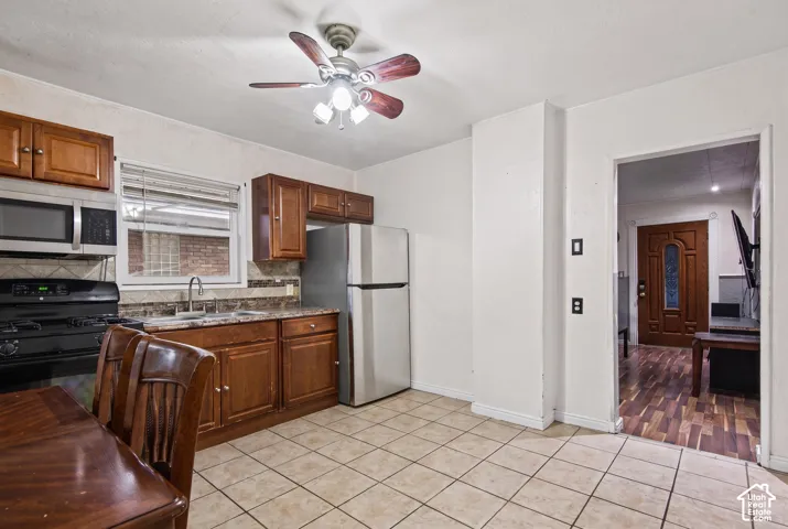 Kitchen featuring wood cabinetry, stainless steel appliances, stone-finish countertops, tiled backsplash, and ceramic floor tile