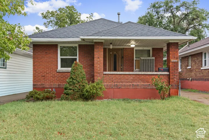 Red brick exterior featuring a covered front porch, masonry pillars, shingled hip roof, and decorative brickwork along the foundation
