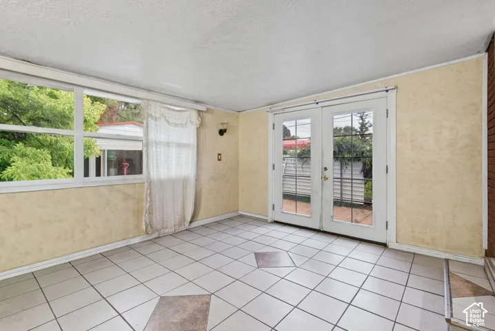 Sunroom featuring ceramic tile flooring with decorative inserts, expansive multi-pane windows, and white French doors