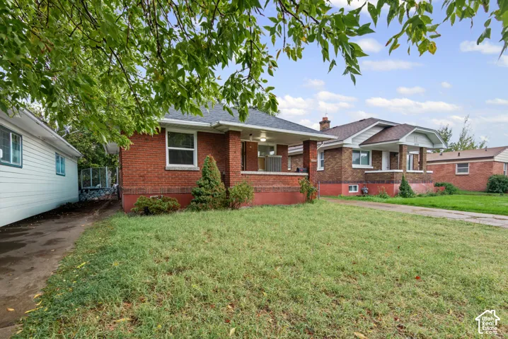 Red brick exterior featuring a covered front porch, concrete driveway, and front lawn
