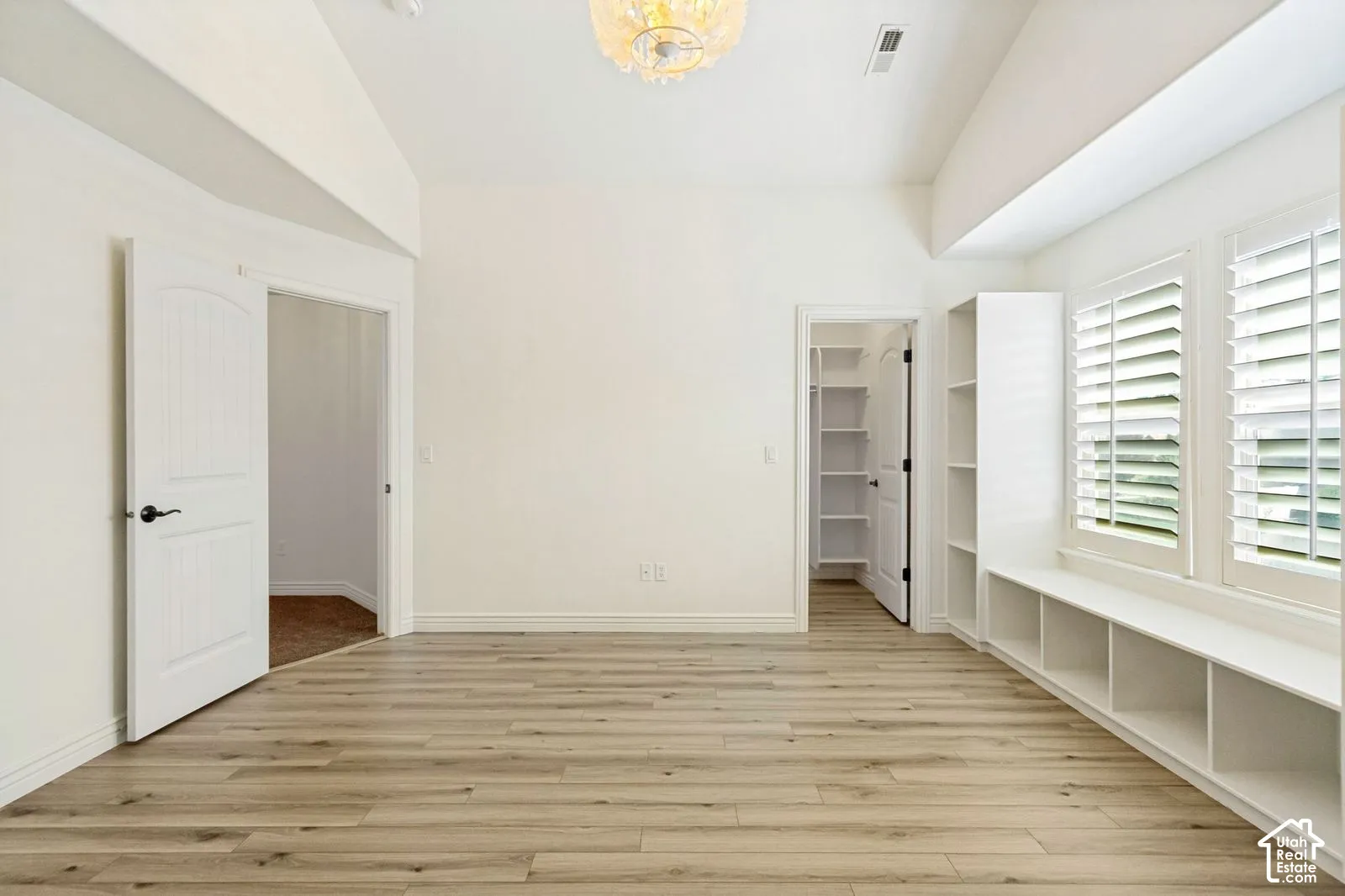 Vaulted ceilings, wood-finish flooring, built-in window seating with shelving, plantation shutters, and an attached walk-in closet with custom shelving