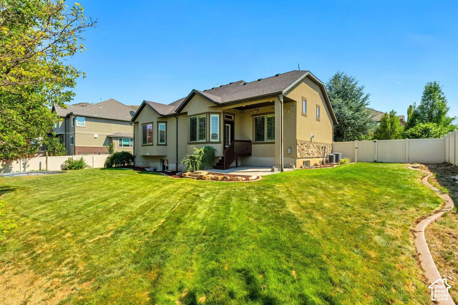 Rear exterior featuring stucco and stone siding, concrete patio, wood-deck stairs, and white vinyl perimeter fencing