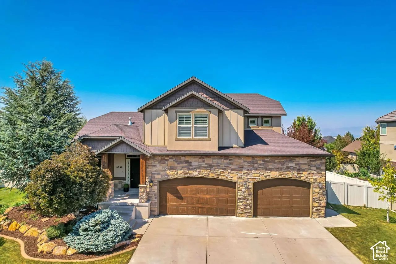 Multi-level residence featuring a stone veneer and vertical siding exterior, dual-bay garage, covered entryway with wood-finish supports, and multi-gabled roofline