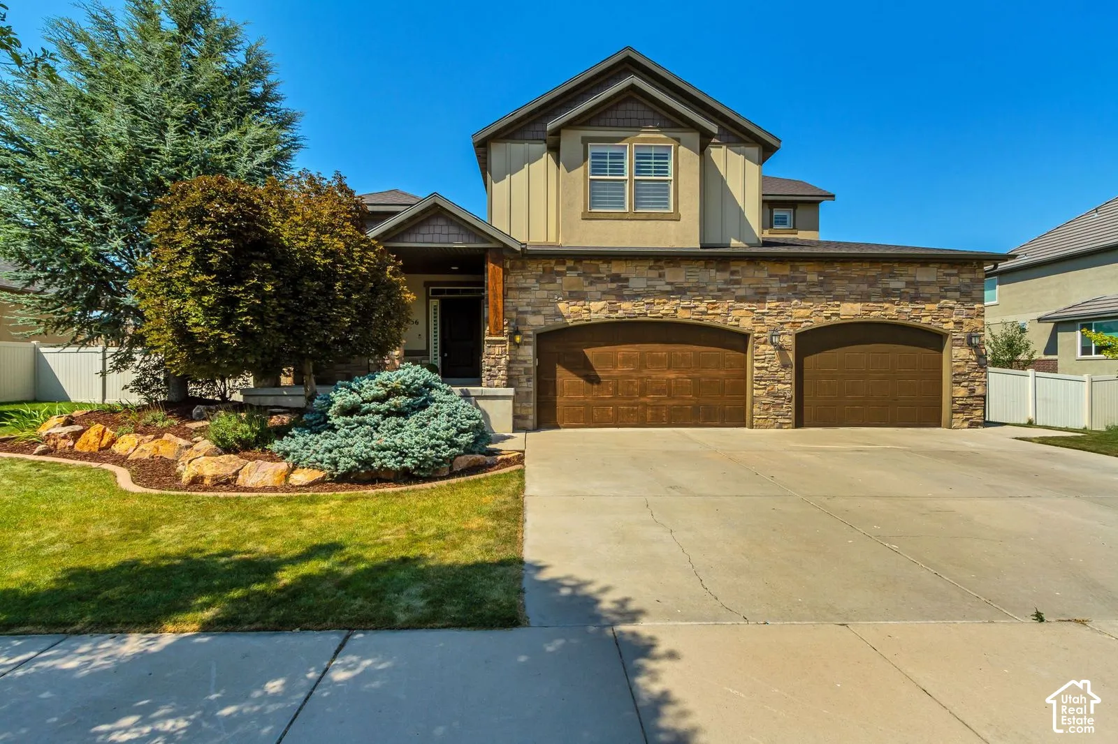 Multi-level exterior featuring a stone facade, vertical siding, two-car garage with arched entries, and professional landscaping with boulder accents