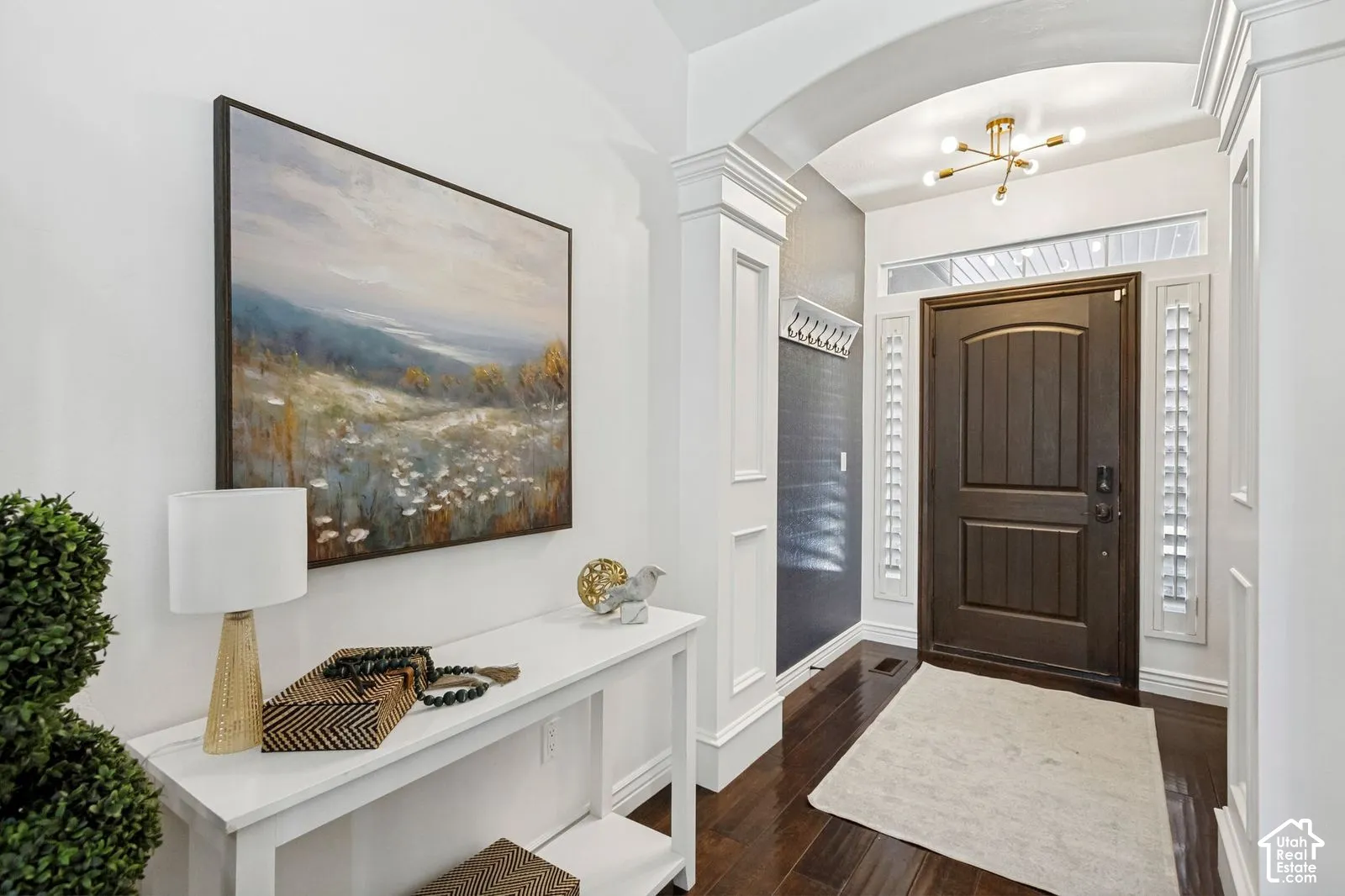 Entryway featuring arched architectural detailing, wood-finish flooring, dark-stained wood door, sidelight windows, and modern multi-arm light fixture