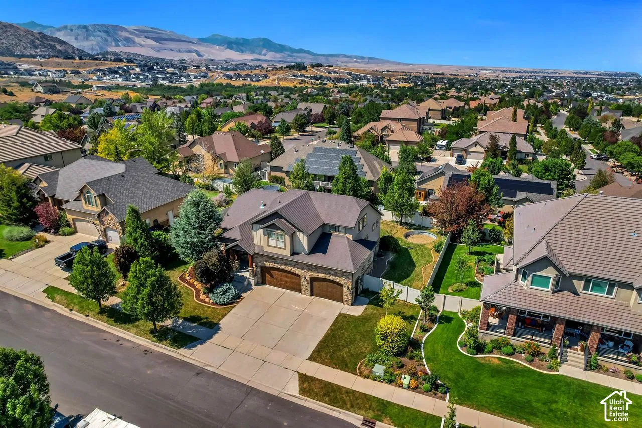 Aerial perspective of a multi-level residence featuring stone and siding exterior, an attached two-car garage, solar panels, and a landscaped lot with mature trees