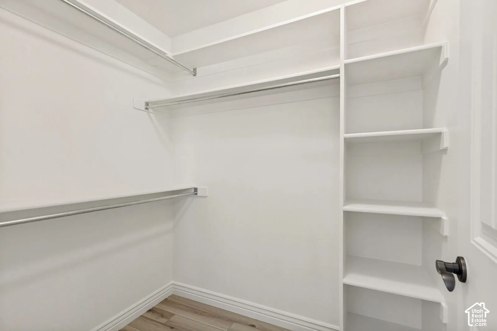 Walk-in closet featuring white built-in shelving, multiple tiered metal garment rods, and wood-finish flooring