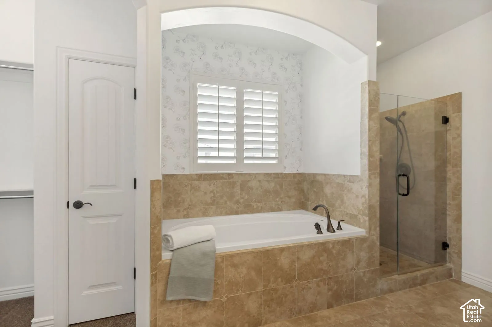 Built-in soaking tub with a tiled surround, arched alcove, plantation shutters, and a walk-in glass-enclosed shower