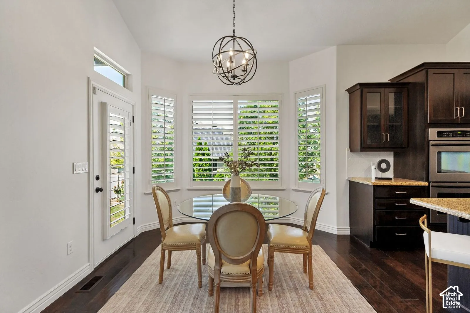 Vaulted ceilings, bay window with plantation shutters, orb-style pendant lighting, dark wood-finish flooring, and built-in wall oven