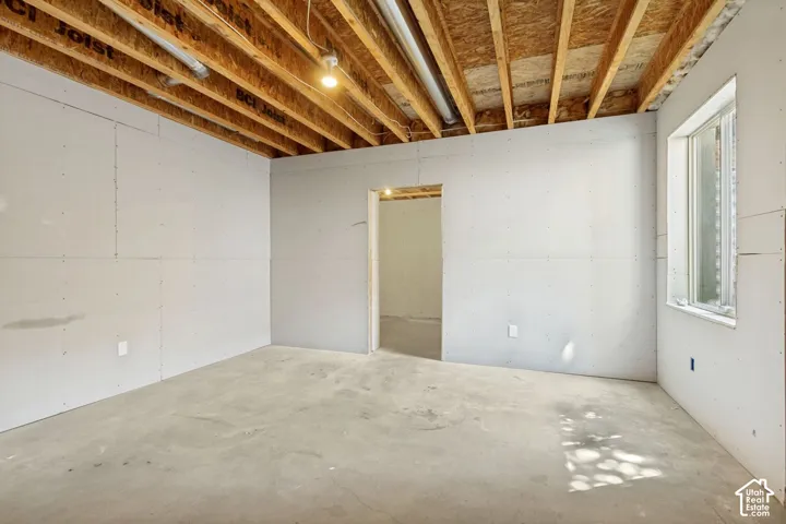 Unfinished space featuring exposed timber joist ceiling, concrete flooring, and perimeter drywall panels