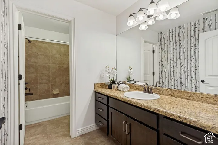 Bathroom featuring a vanity with stone-finish countertop, undermount sink, and dark-toned cabinetry, paired with a full-width wall mirror and six-light vanity fixture