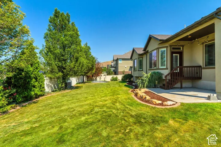 Rear yard featuring a concrete patio, elevated wooden deck, stone-bordered mulch beds, and mature landscaping