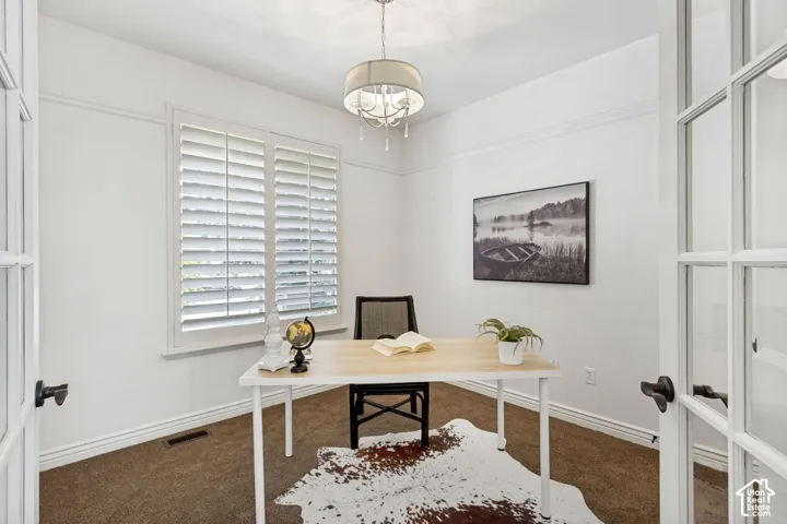 Interior space featuring French doors, white plantation shutters, neutral carpeting, and a drum-style chandelier with crystal accents