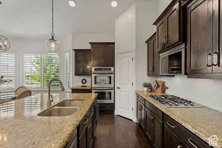 Kitchen featuring dark-finish cabinetry, natural stone countertops, stainless steel built-in double wall ovens, gas cooktop, and wood-finish flooring