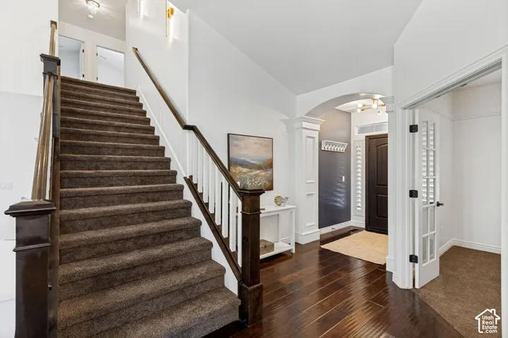 Foyer featuring wood-finish flooring, staircase with a dark wood handrail and white balusters, arched entryway, and double French doors with glass panes