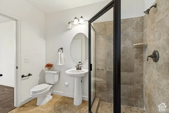 Bathroom featuring a pedestal sink with an oval mirror, three-light vanity fixture, and a tiled shower stall with a black metal-framed glass door and bronze-tone hardware