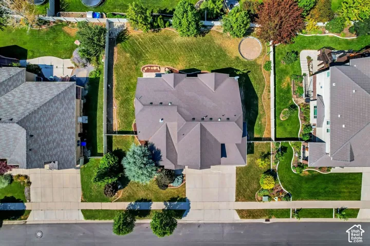 Aerial view featuring a multi-pitched asphalt shingle roof, concrete driveway, fenced-in backyard, and mature landscaping
