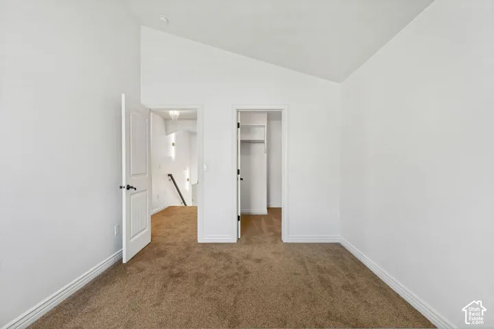 Vaulted ceiling, neutral wall-to-wall carpeting, and walk-in closet with built-in shelving