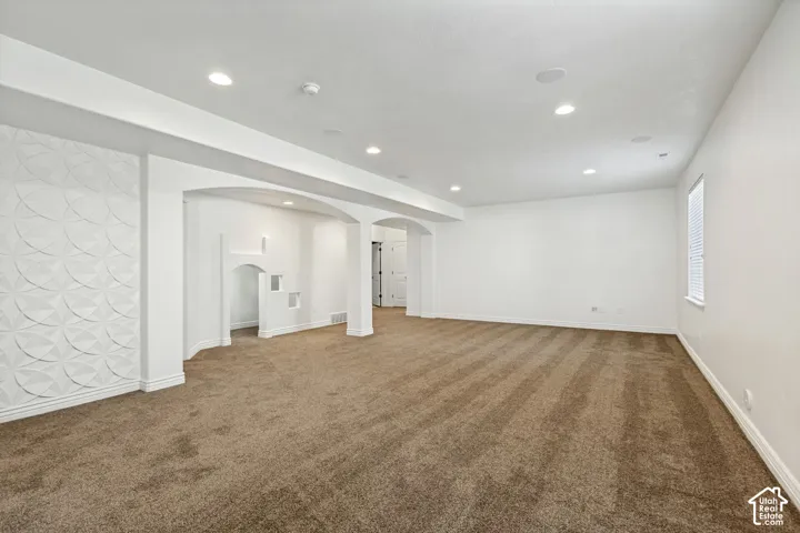 Spacious interior featuring recessed lighting, architectural arched pillars, and a textured geometric accent wall