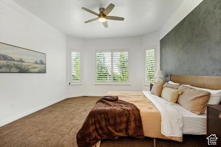 Bay window featuring plantation shutters, textured accent wall, crown molding, and ceiling fan