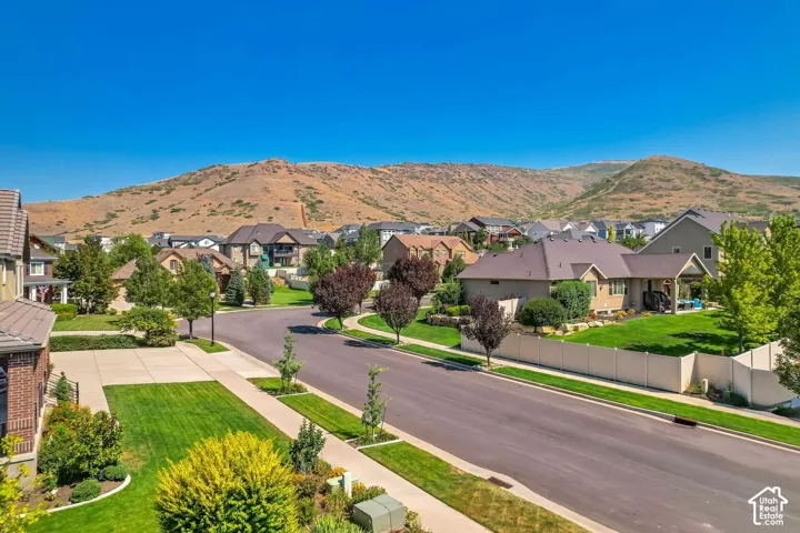 Suburban neighborhood featuring asphalt streets, concrete sidewalks, landscaped yards, mature trees, and mountain scenery