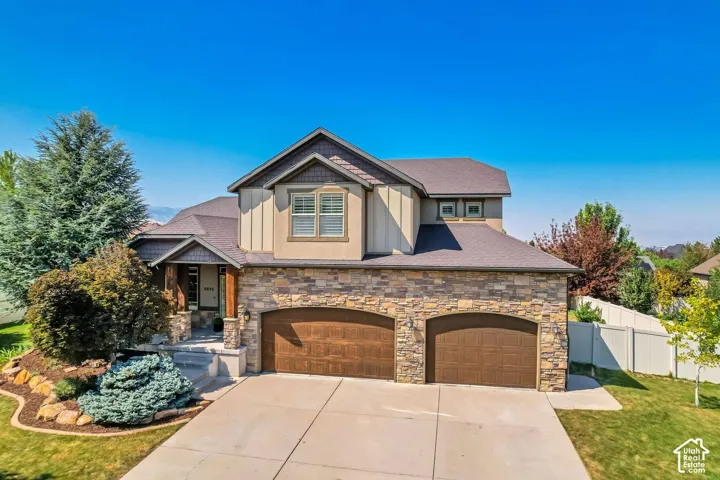 Multi-level exterior featuring a stone masonry facade, board-and-batten siding, dual-bay garage, covered entrance with timber post accents, and a concrete driveway