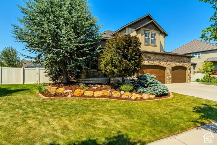 Exterior featuring a stone facade, arched garage entryways, wood-finish garage doors, and landscaped front yard with stone edging