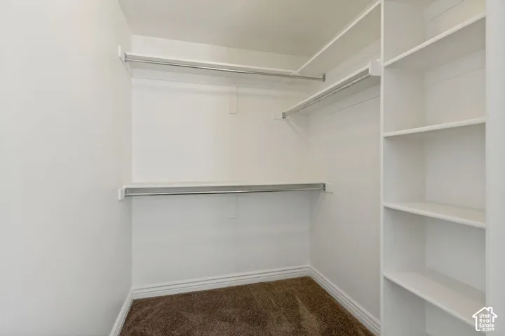 Walk-in storage space featuring custom white built-in shelving and multi-level metal hanging rods