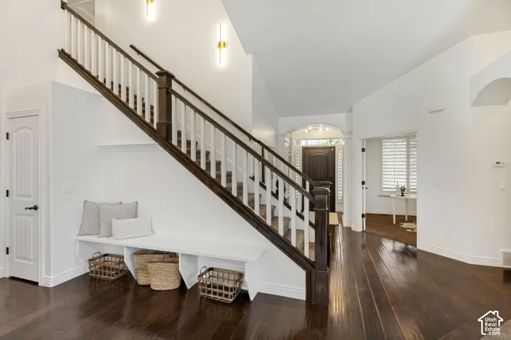 Foyer featuring dark wood-finish flooring, a built-in staircase bench, a two-tone staircase with a stained wood handrail, and wall-mounted brass light fixtures