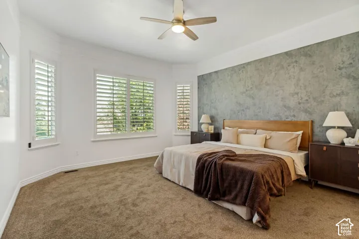 Bedroom featuring a textured accent wall, crown molding, plantation shutters, and a ceiling fan