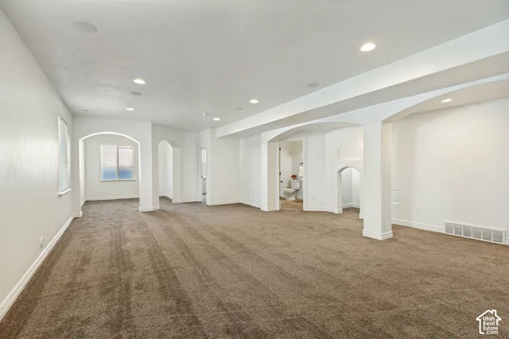 Open-concept interior featuring recessed lighting, plush wall-to-wall carpeting, decorative arched room dividers, and integrated ceiling speakers