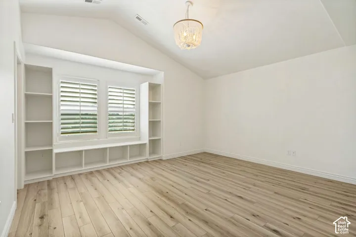Vaulted ceiling, wood-finish flooring, built-in shelving with integrated storage bench, plantation shutters, and ornate pendant lighting