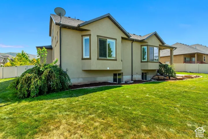 Exterior featuring stucco siding, double-bay windows, a shingle roof, and a fenced backyard with mature landscaping
