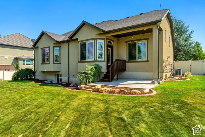 Stucco and stone exterior featuring a concrete patio, covered deck, bay windows, and a landscaped lawn with rock borders
