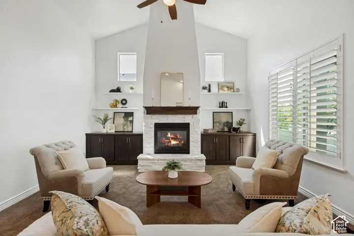 Vaulted ceilings, floor-to-ceiling fireplace with stone detailing and a dark wood mantel, built-in cabinetry, floating wall shelves, and shutter window coverings