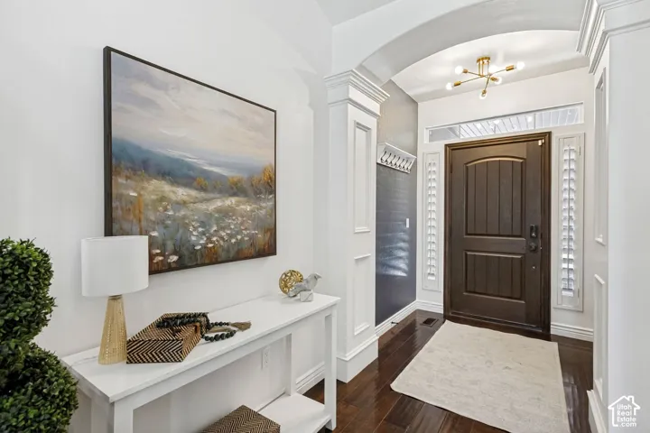 Entryway featuring arched architectural detailing, wood-finish flooring, dark-stained wood door, sidelight windows, and modern multi-arm light fixture